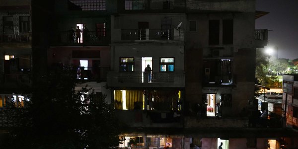 Building with lights switched off and residents coming out in balcony with candles and diya